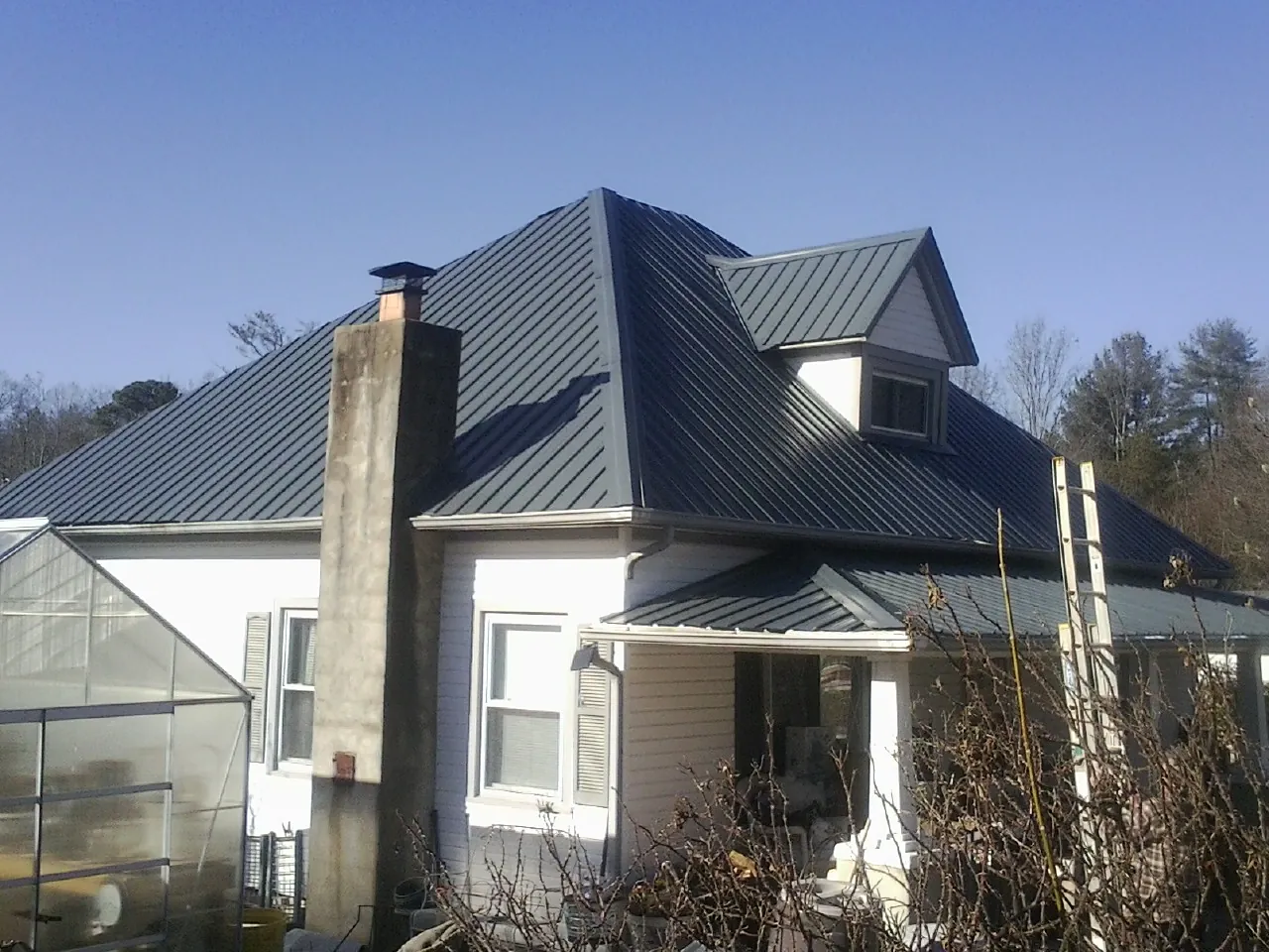 Dark blue standing seam metal roof on a white farmhouse with dormer — Slate & Tile Roof Repair by Roofing Brothers in Zimmerman