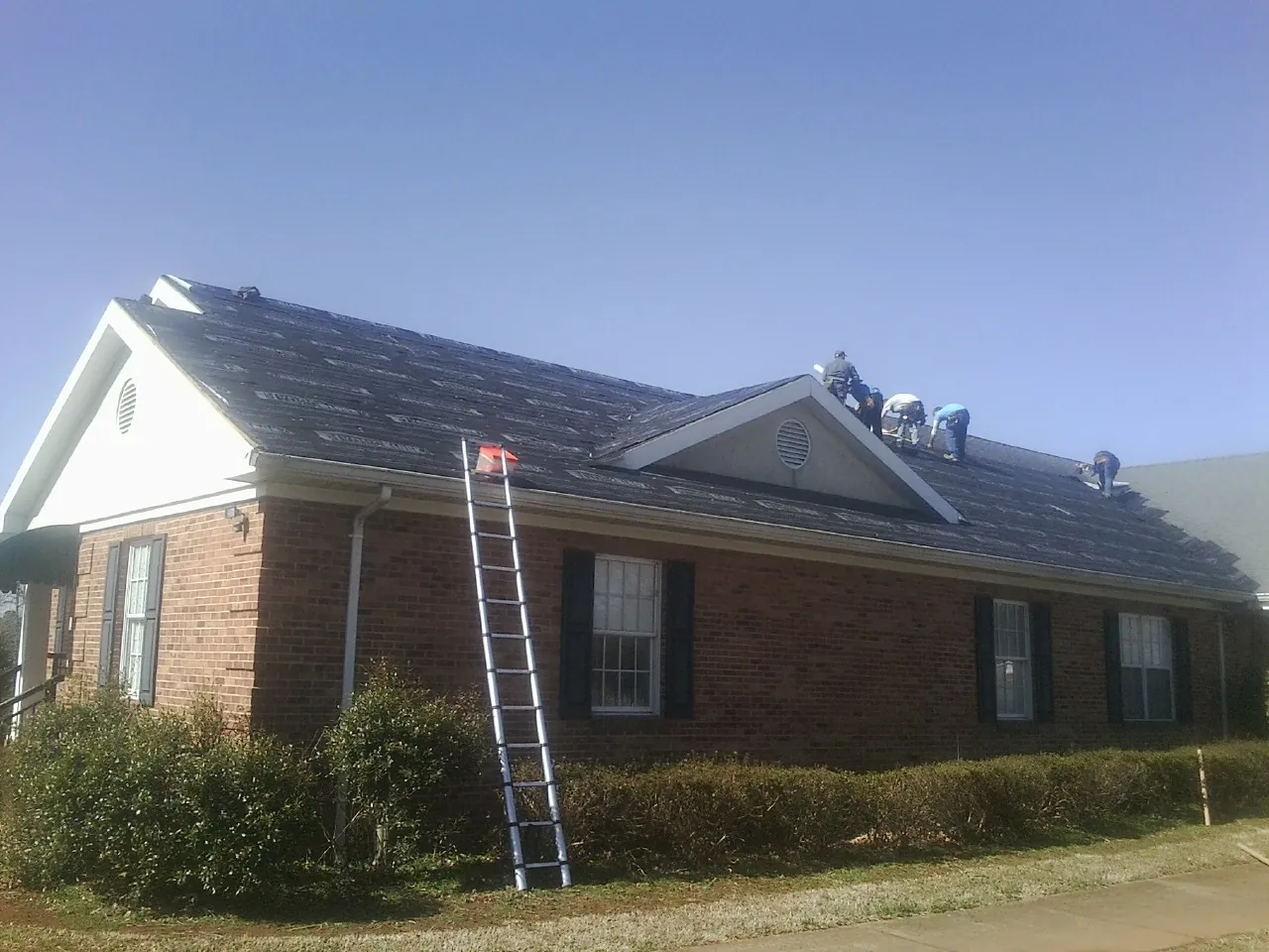 Crew tearing shingles off a brick ranch roof with a ladder set — Emergency Roof Repair work by our crew in Zimmerman