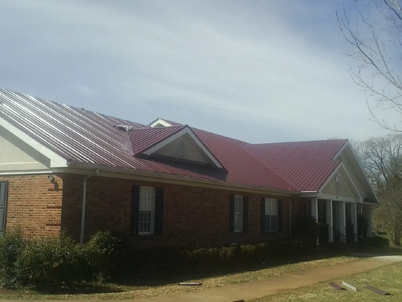 Red metal roof with gabled entries on a long brick building, from a Hail Damage Roof Repair job in Zimmerman