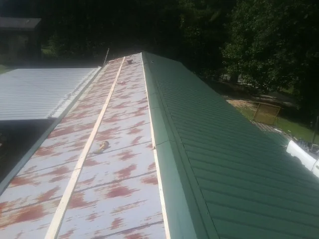 Old rusted panels beside newly installed green metal roofing — Wind Damage Roof Repair by Roofing Brothers in Zimmerman