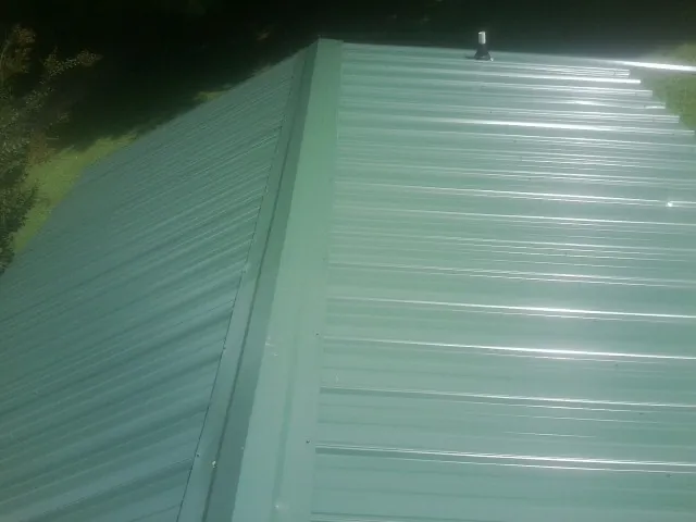 New green metal panels meeting at the ridge of a roof — Flat Roof Repair work by our crew in Zimmerman
