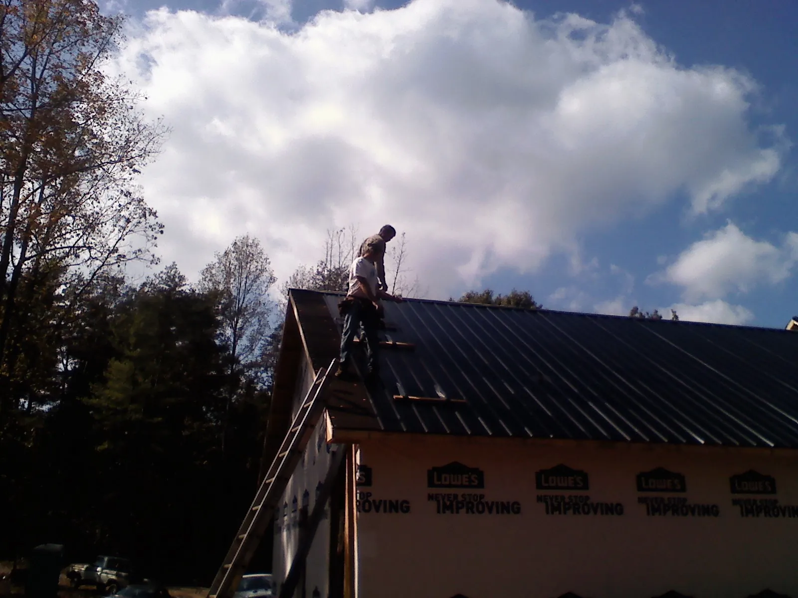 Roofer fastening dark metal panels high against a cloudy sky, from a Roof Inspection job in Zimmerman