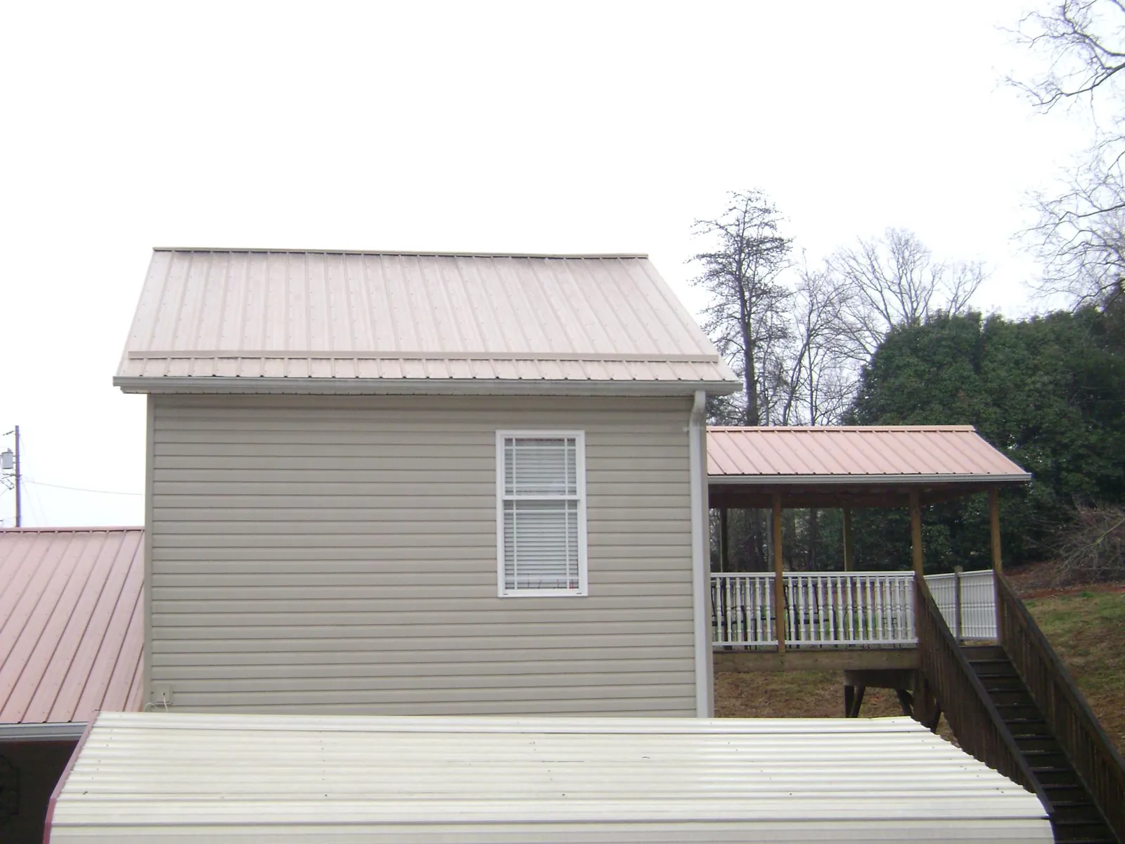 Tan metal roofs on a two story addition and attached porch, from a Roof Replacement job in Zimmerman